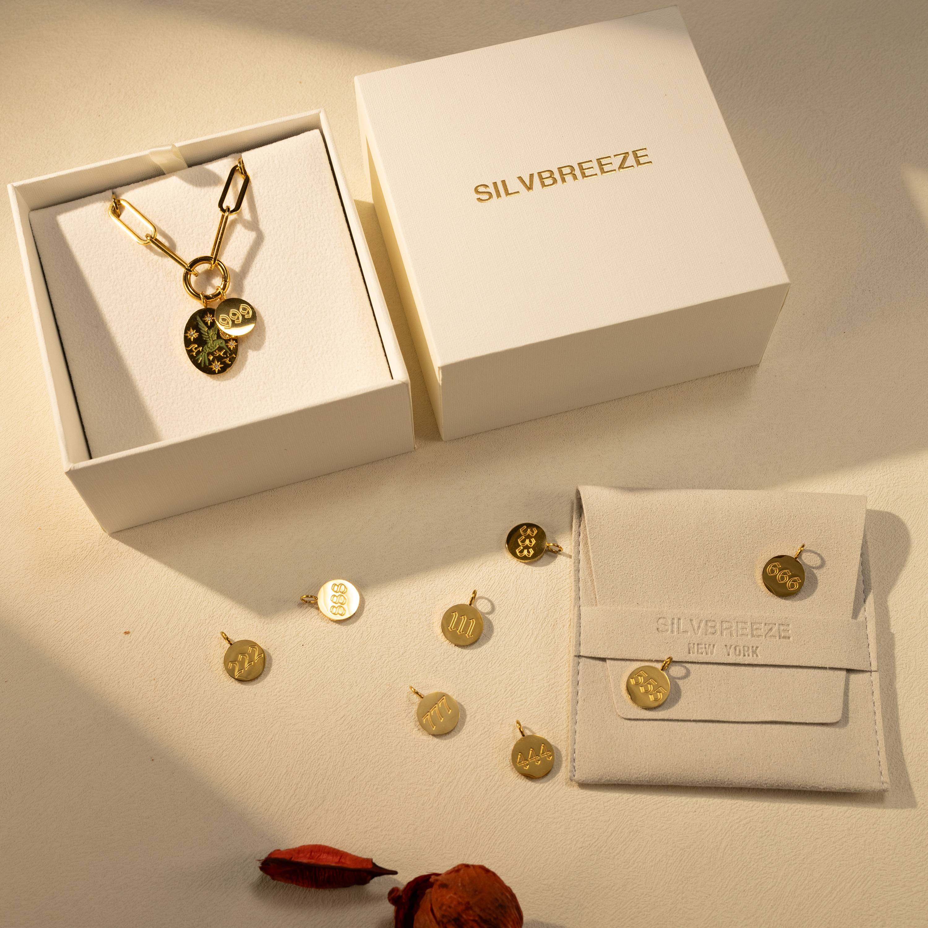 Silvbreeze paperclip O-clasp necklace with bluebird and angel number 999 charms displayed with gift boxes and packaging in a styled flatlay.