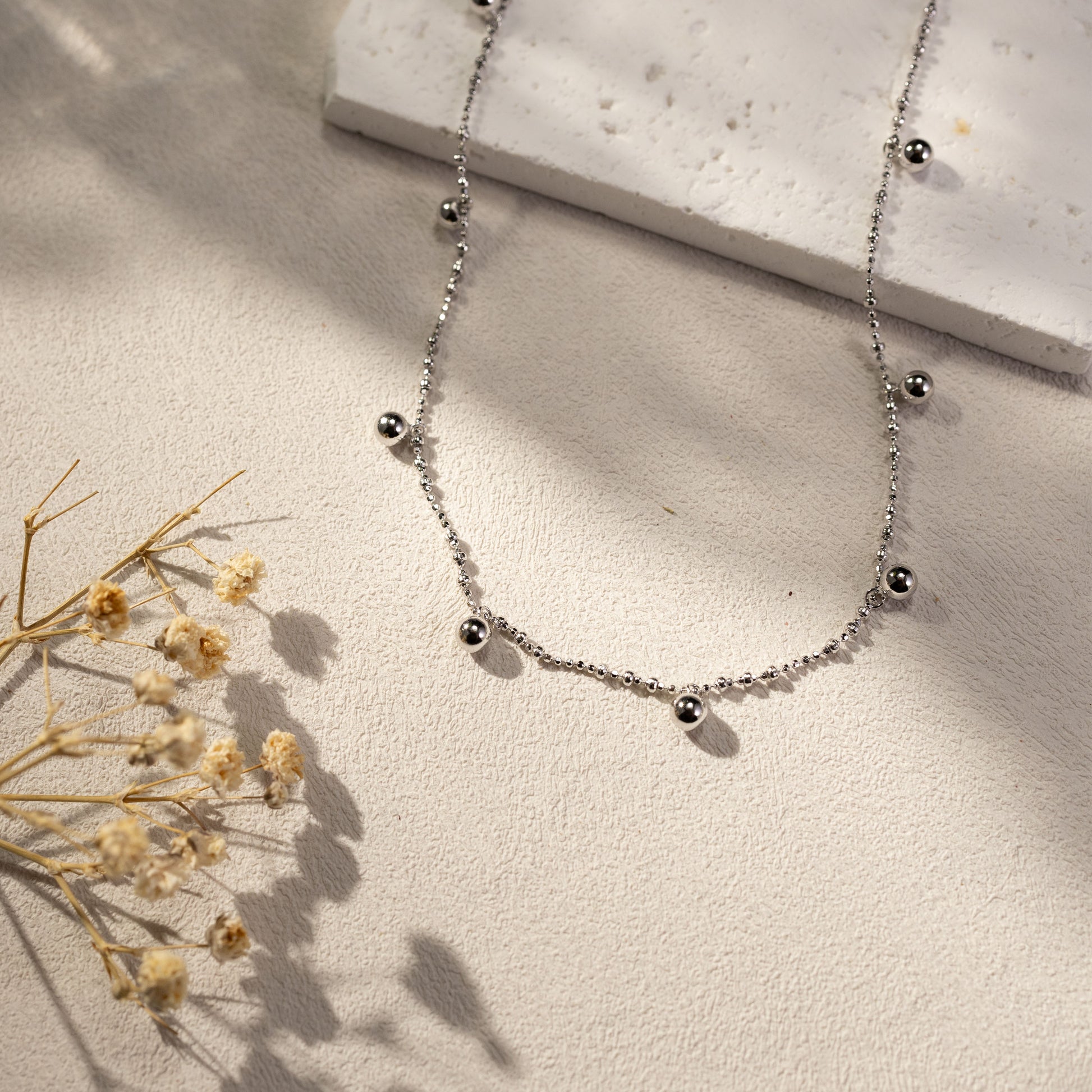Silvbreeze silver ball bead necklace lifestyle scene photo with soft daylight shadow on textured background