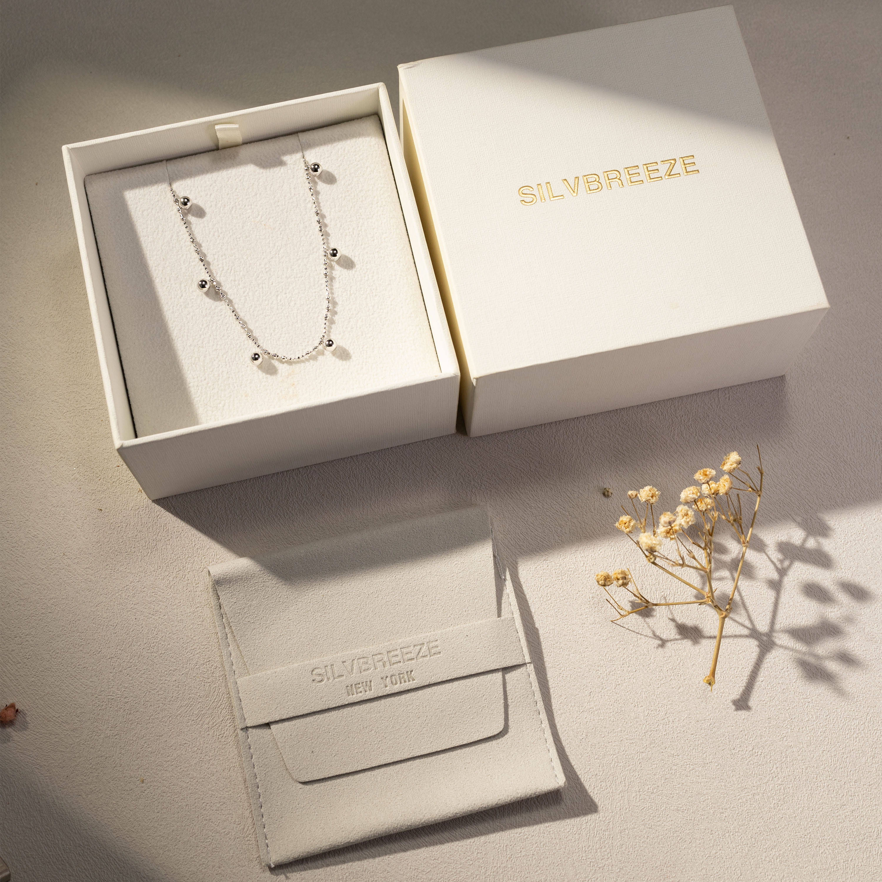 Silver beaded necklace displayed inside Silvbreeze gift box with branded packaging and dried floral decor in soft natural light.
