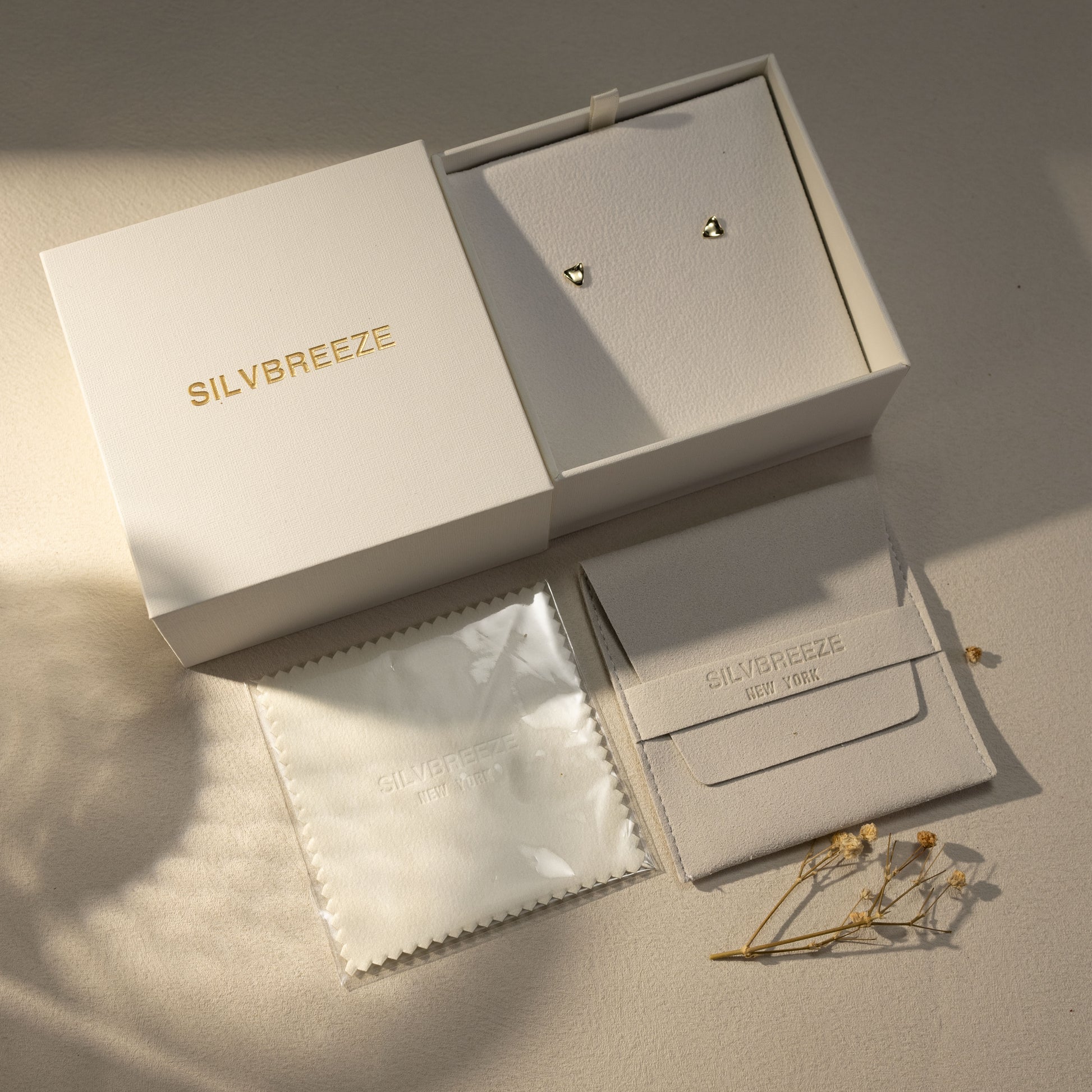 Tria 14K gold vermeil triangle stud earrings presented in a premium Silvbreeze gift box with suede pouch and polishing cloth, styled in warm natural light to highlight luxury jewelry packaging