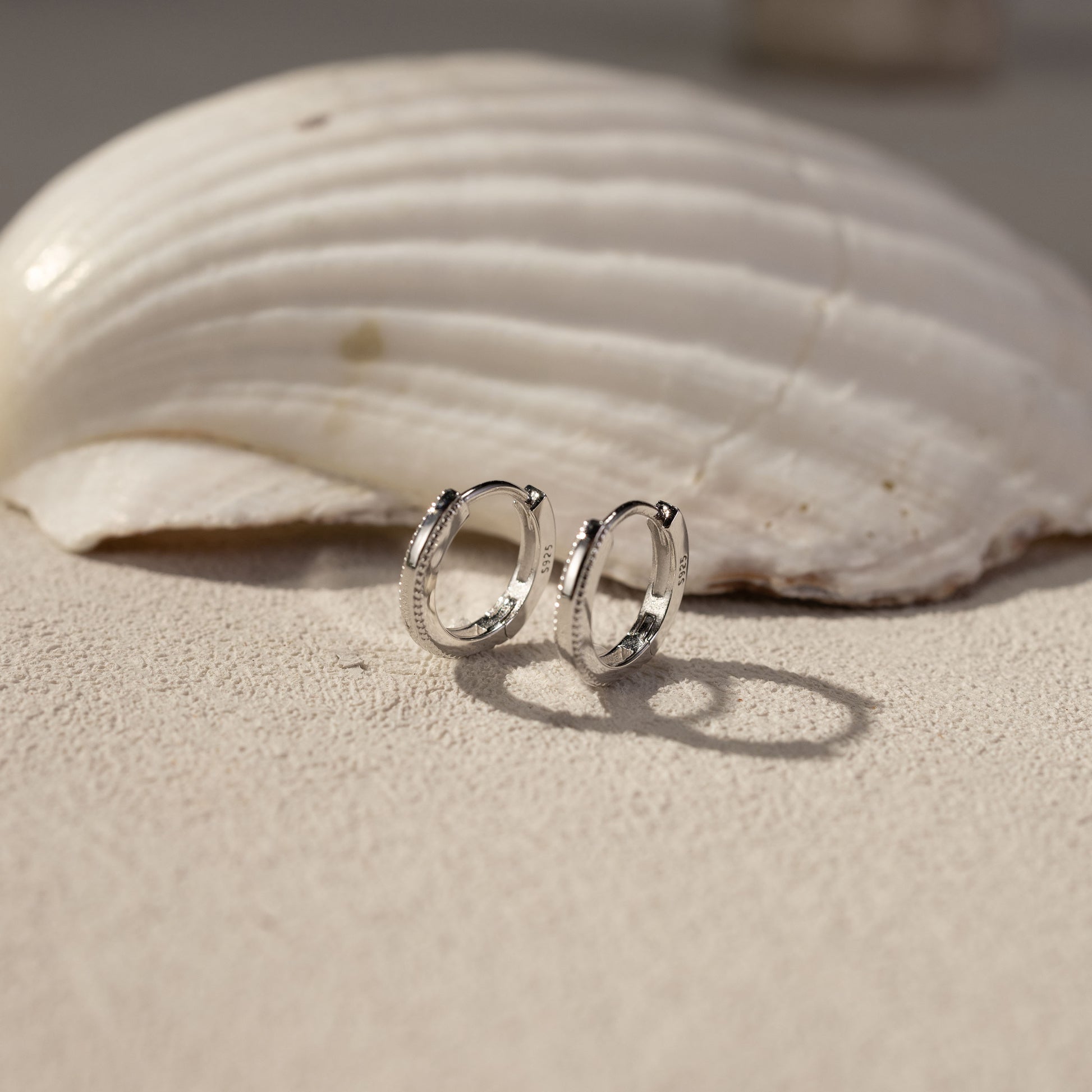 White gold vermeil Onita huggie earrings on textured surface with shell, lightweight tarnish-resistant hoop earrings by Silvbreeze