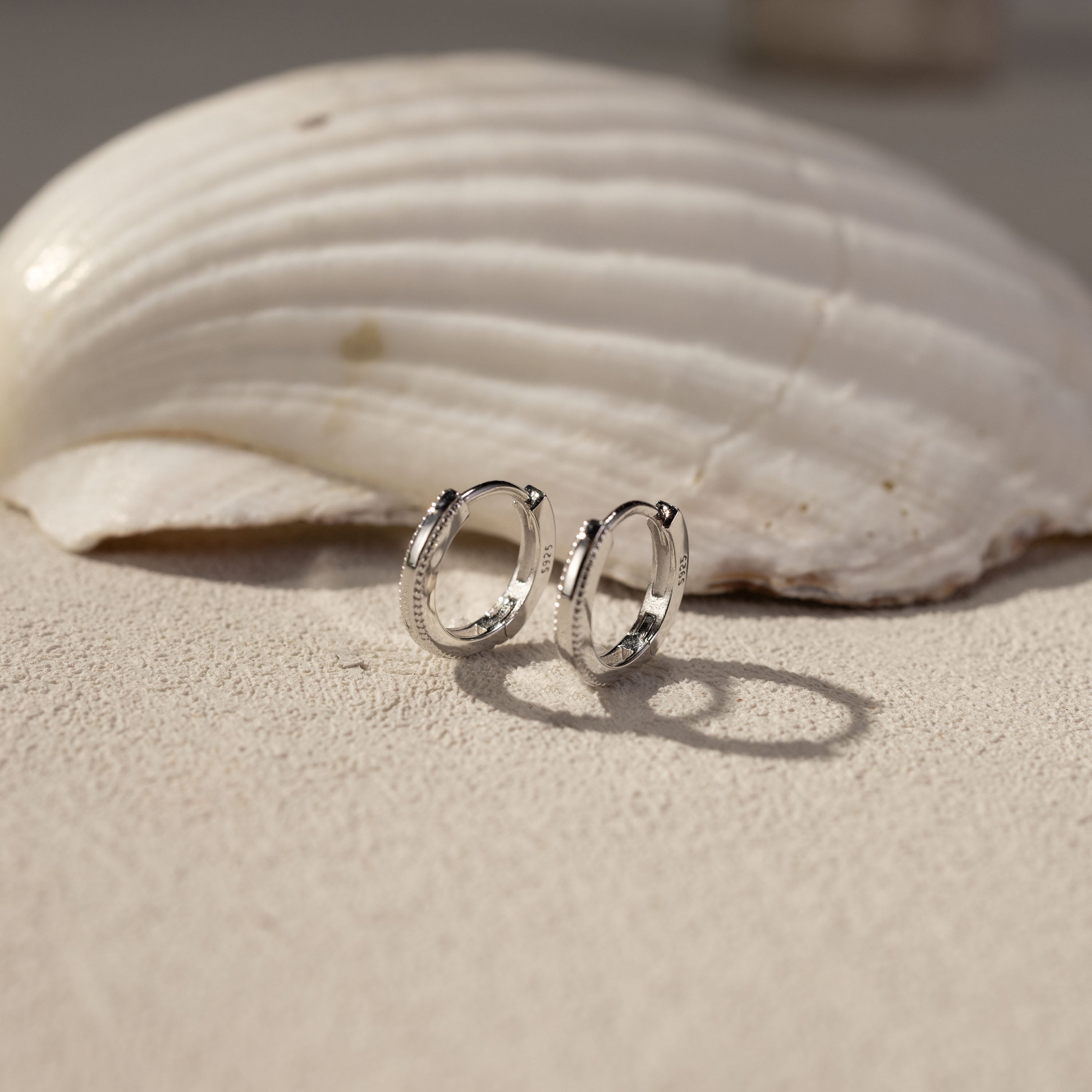 White gold vermeil Onita huggie earrings on textured surface with shell, lightweight tarnish-resistant hoop earrings by Silvbreeze
