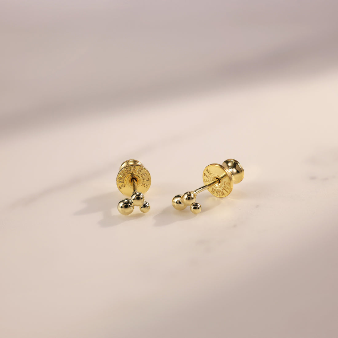 Minimalist gold and silver stud earrings laid out on soft fabric, designed for comfortable daily wear in an active lifestyle.